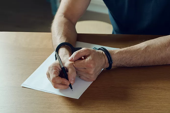 Man in handcuffs writing on paper regarding false accusation of domestic violence