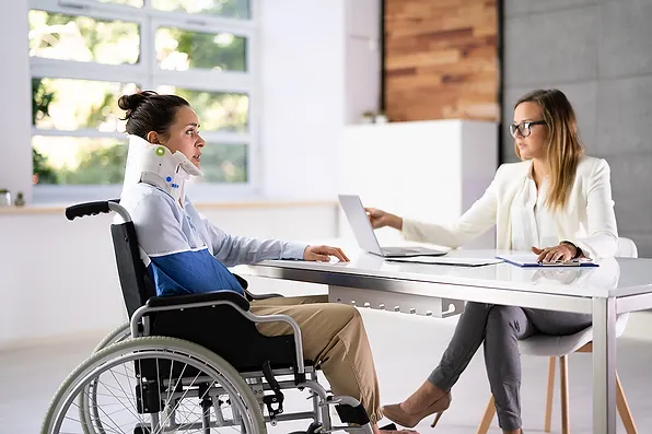 Image of women in neck brace in wheel chair with woman at table