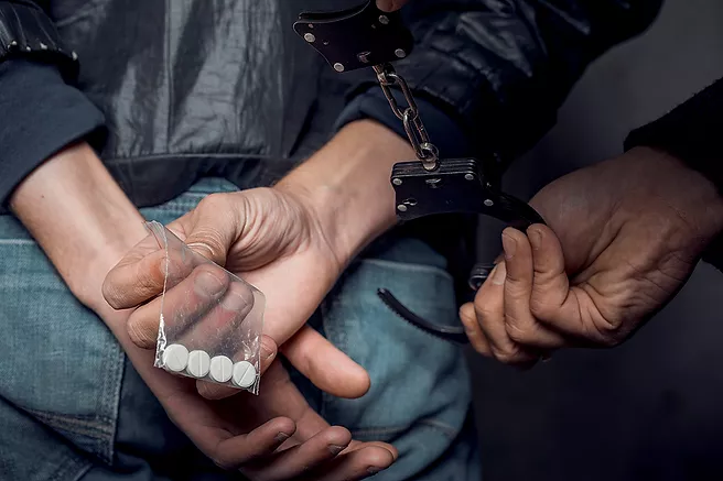Image of man being handcuffed with drugs in his hand representing Drug Possession Crime