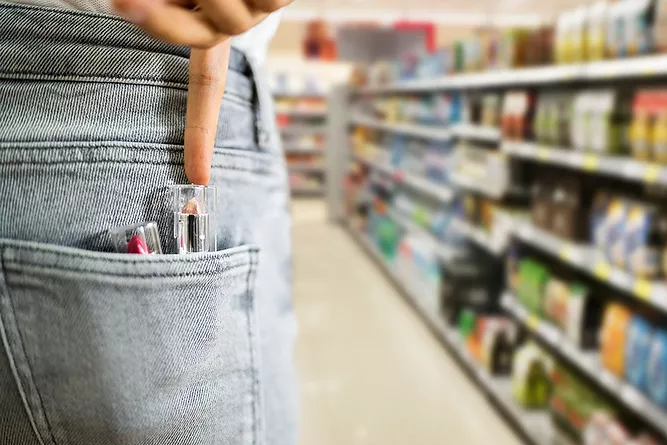 Image shows a person slipping a tube of makeup into their back pocket in a store in a probable theft crime